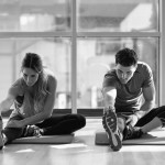 Two people streching their legs in gym. Young woman and man working out indoors. Two people streching their legs on the floor of a gym.