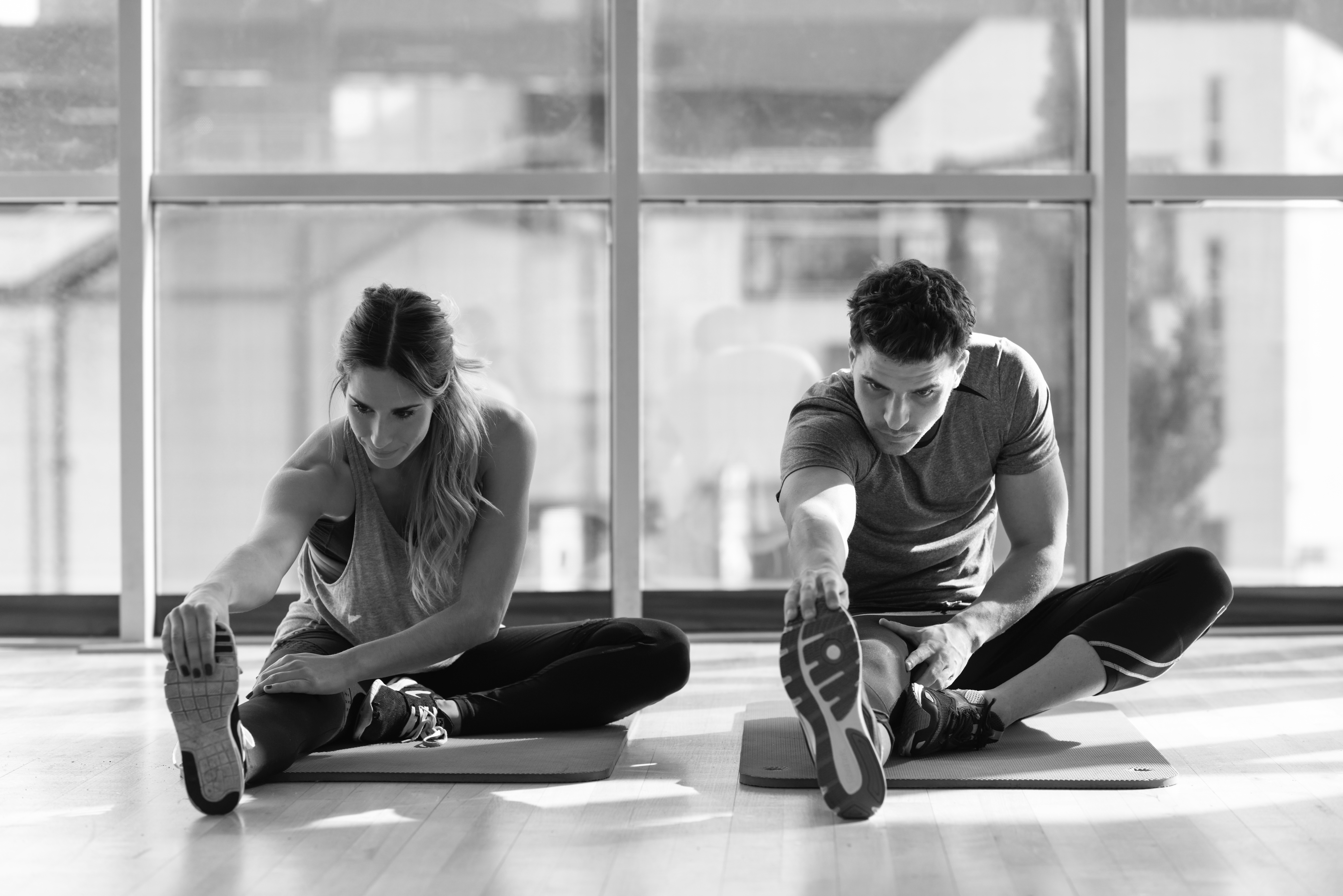 Two people streching their legs in gym. Young woman and man working out indoors. Two people streching their legs on the floor of a gym.