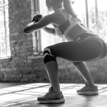Young fit sporty active athlete woman wear sportswear crouching doing squats session fitness training legs buttocks muscles workout exercise in modern sunny gym space indoors, rear back close up view
