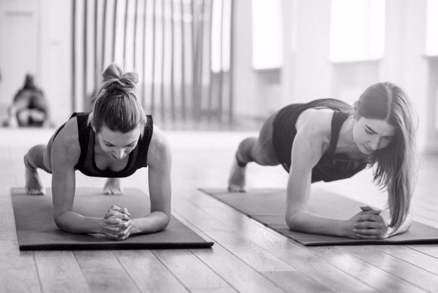 Front view of two sporty fit and slim middle aged women doing planking exercise indoors together with a natural light in modern interior sport studio hall or yoga class. Front view of two sporty fit and slim middle aged women doing planking exercise indoors together with a natural light in modern interior sport studio hall or yoga class.