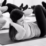 Group of young sporty people doing crisscross Attractive woman and group of young sporty people practicing in sport gym, doing crisscross pose, bicycle crunches exercise, working out, indoor full length, students training in fitness club, studio